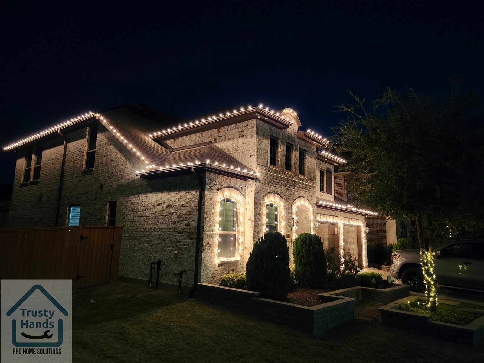 Two-story stone home in Katy, TX with warm white Christmas roofline and arch lighting installed by Trusty Hands