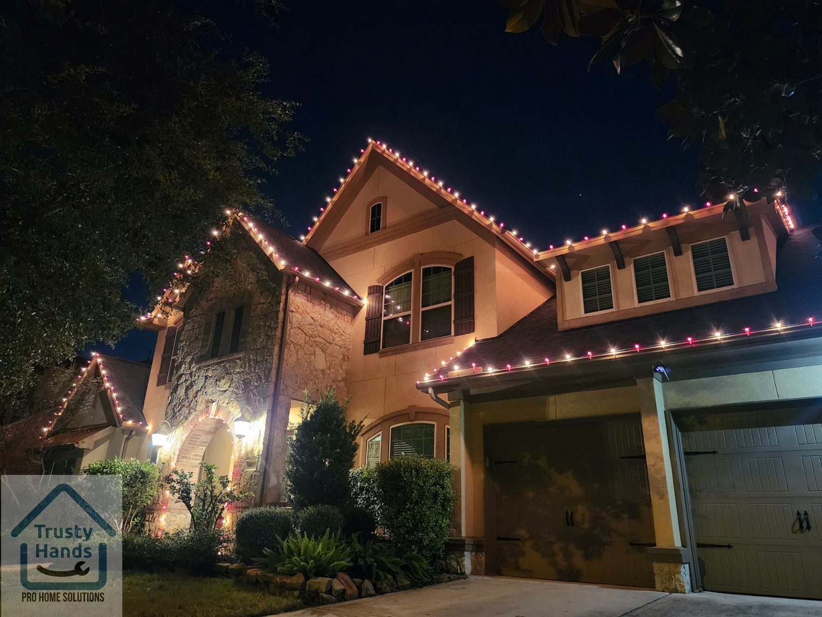 Two-story home with red and warm white Christmas roofline lighting and lit tree, Katy TX
