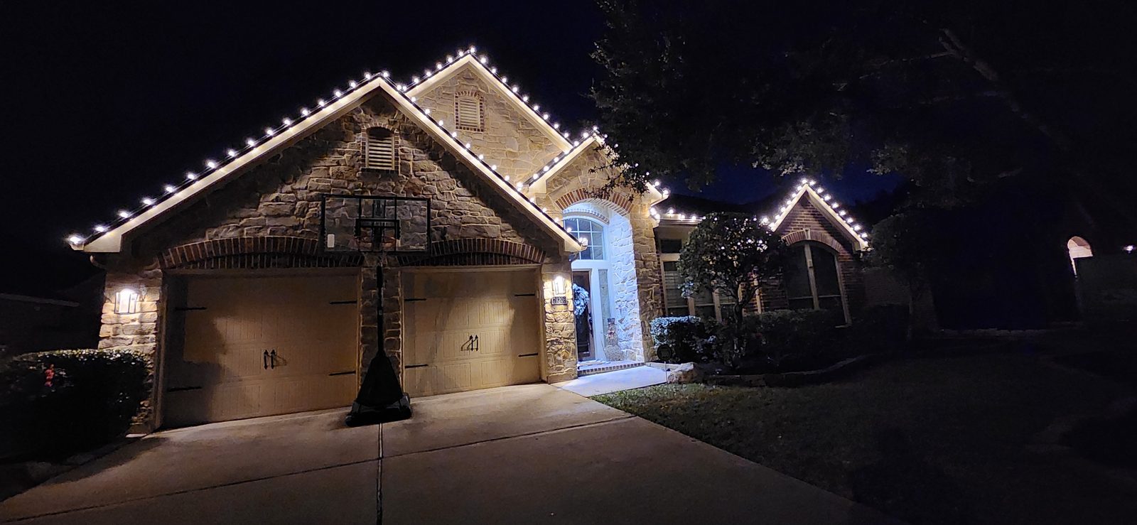 One-story stone home in Katy, TX with warm white Christmas roofline lighting