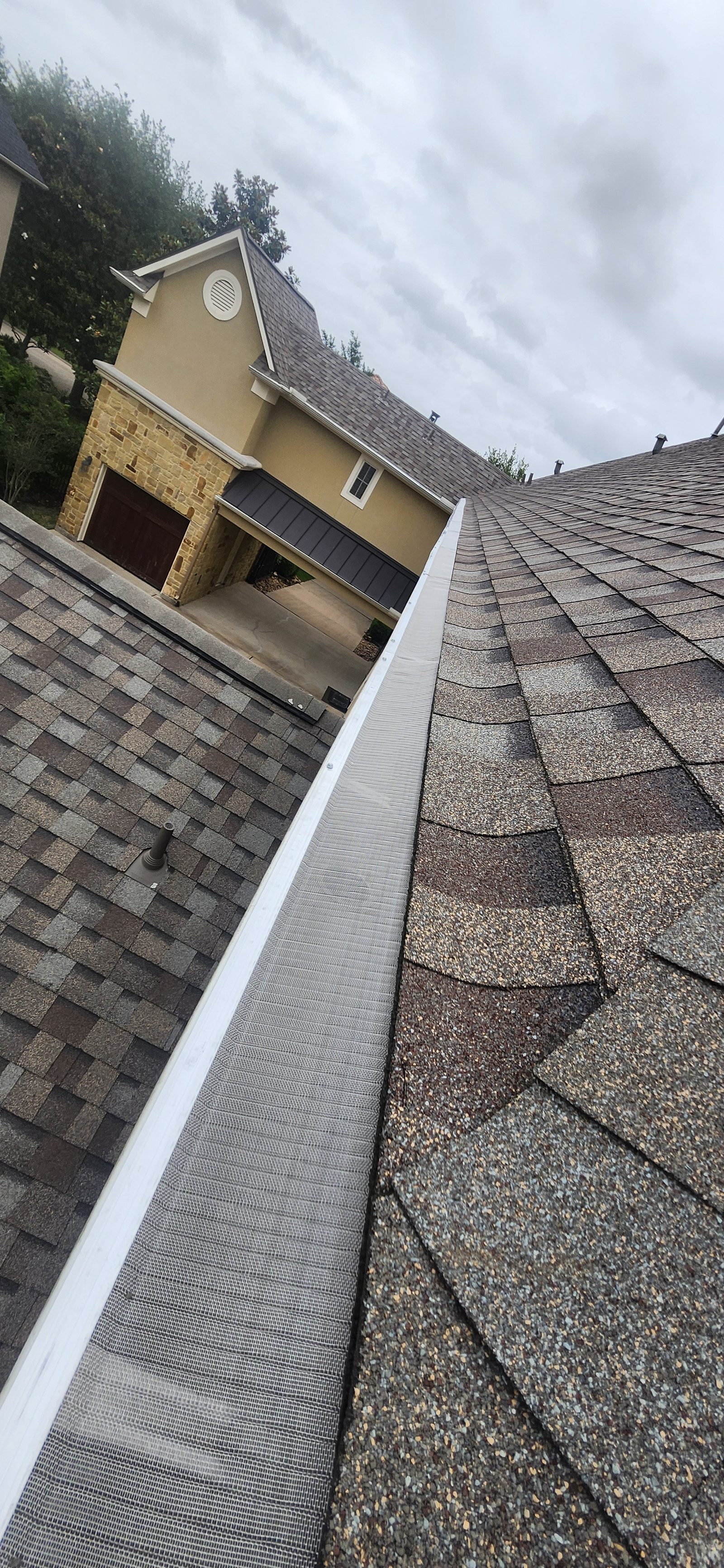 Gutter guard installed along a roofline with a two-story home in the background, Katy TX