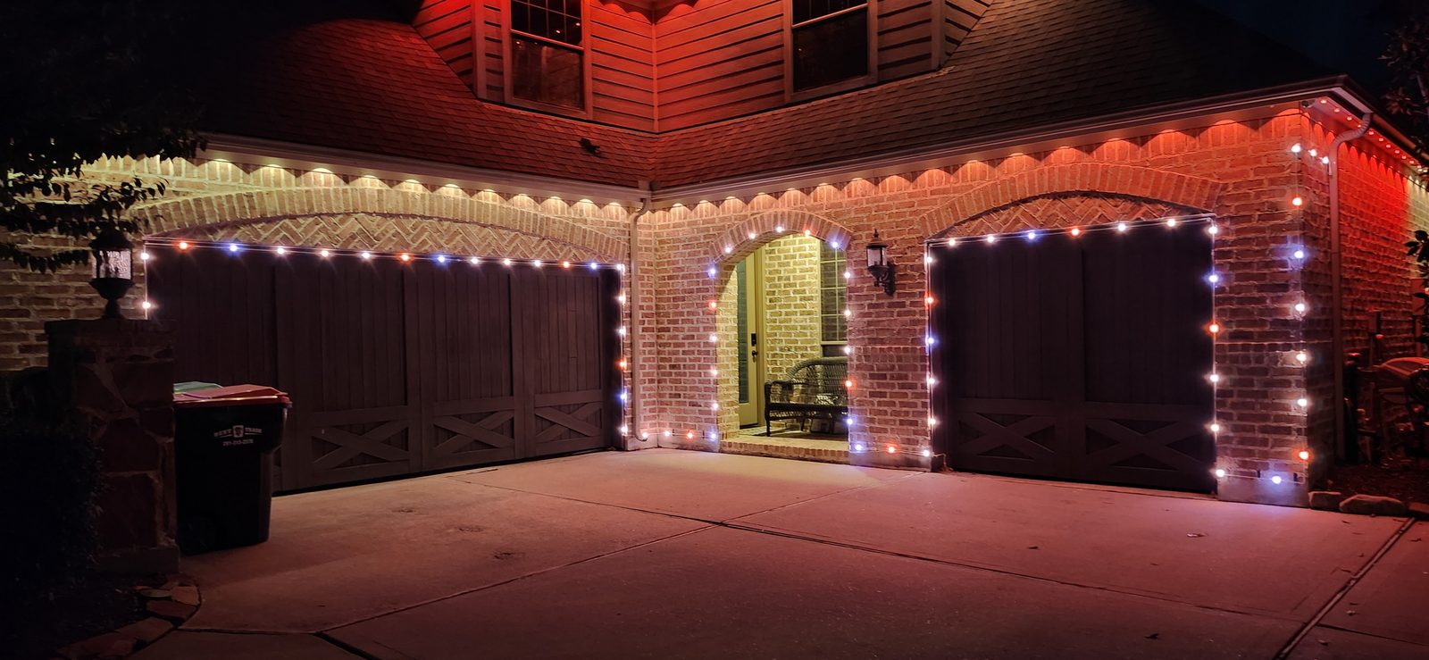 Red and white permanent outdoor accent lighting along a garage roofline in Katy, TX