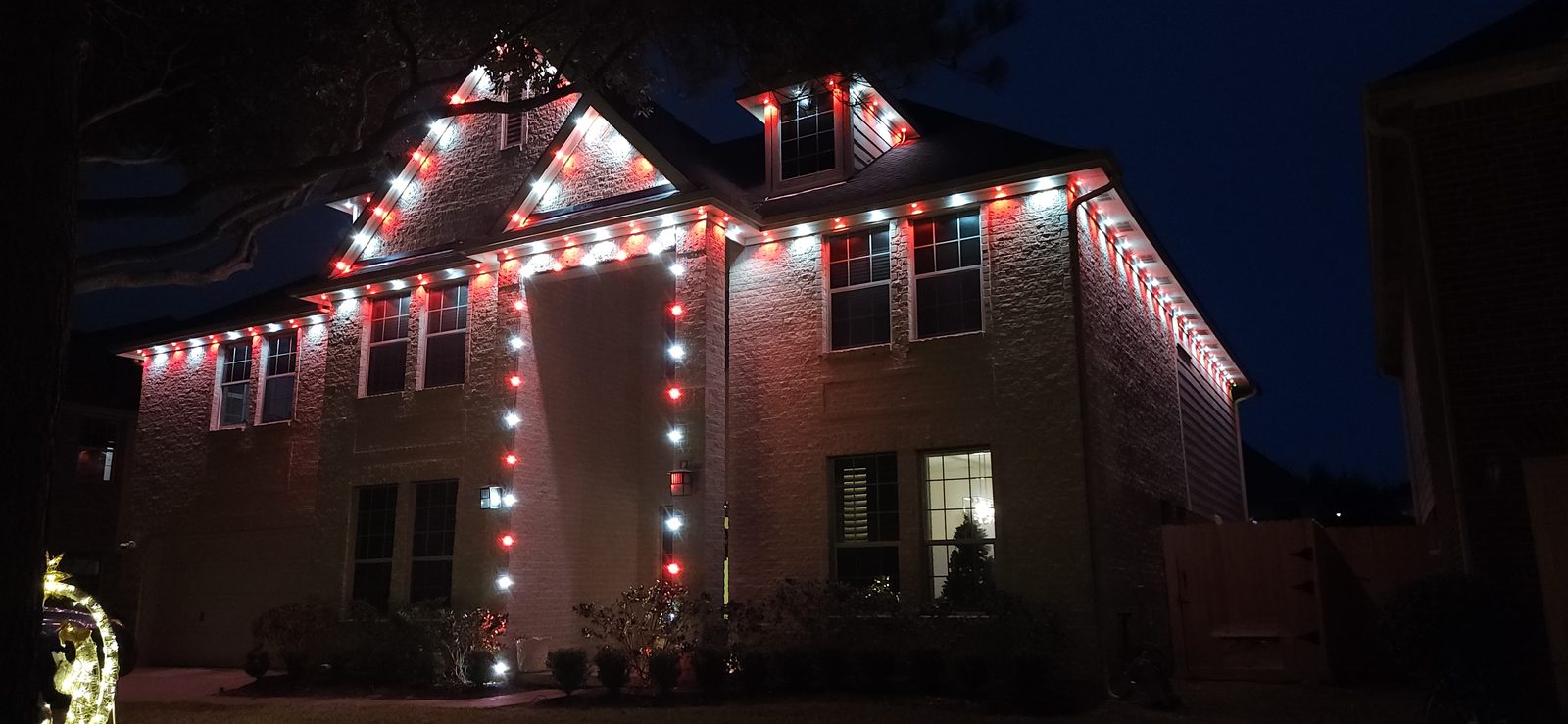 Red and white permanent roofline lighting on a two-story home exterior in Katy, TX
