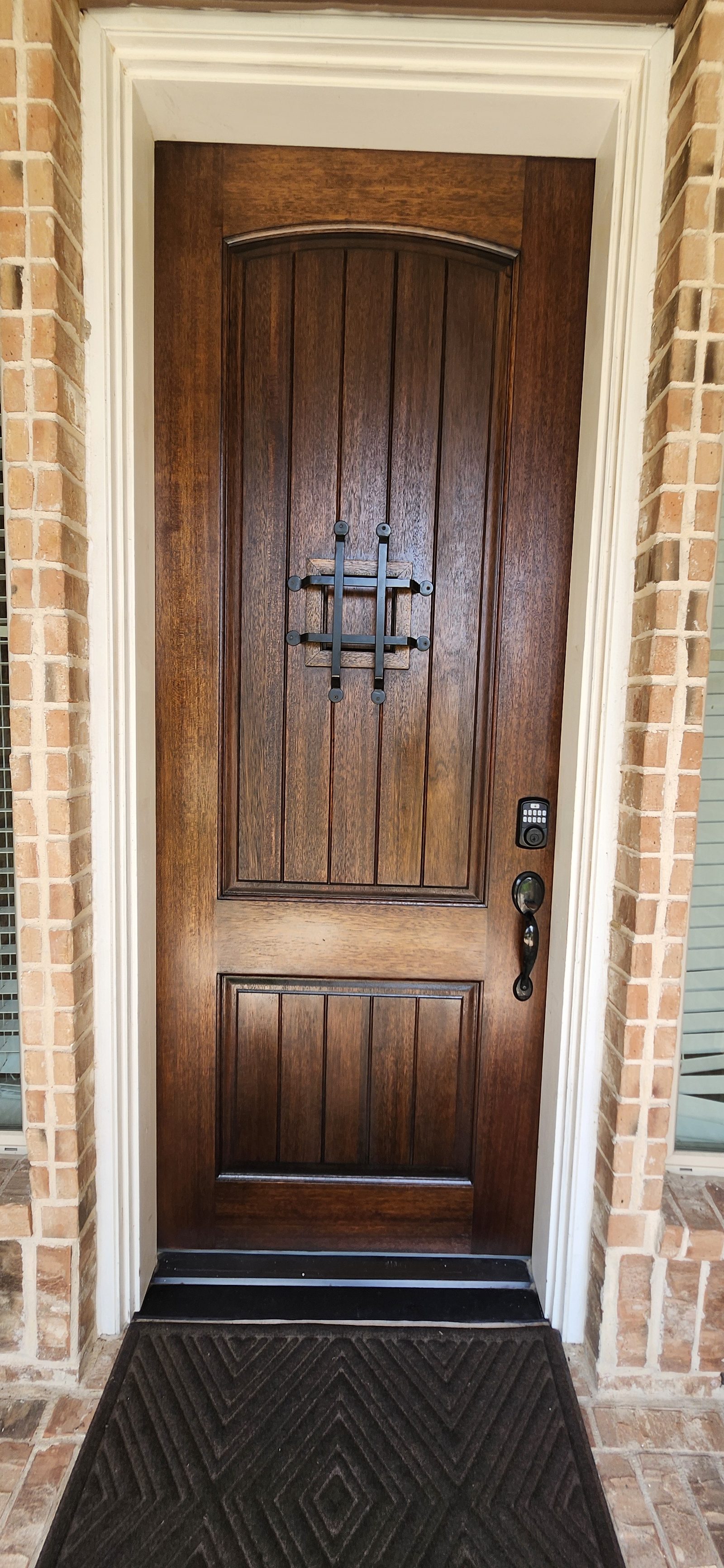 Stained wood front door with iron grille and keypad lock in Katy, TX