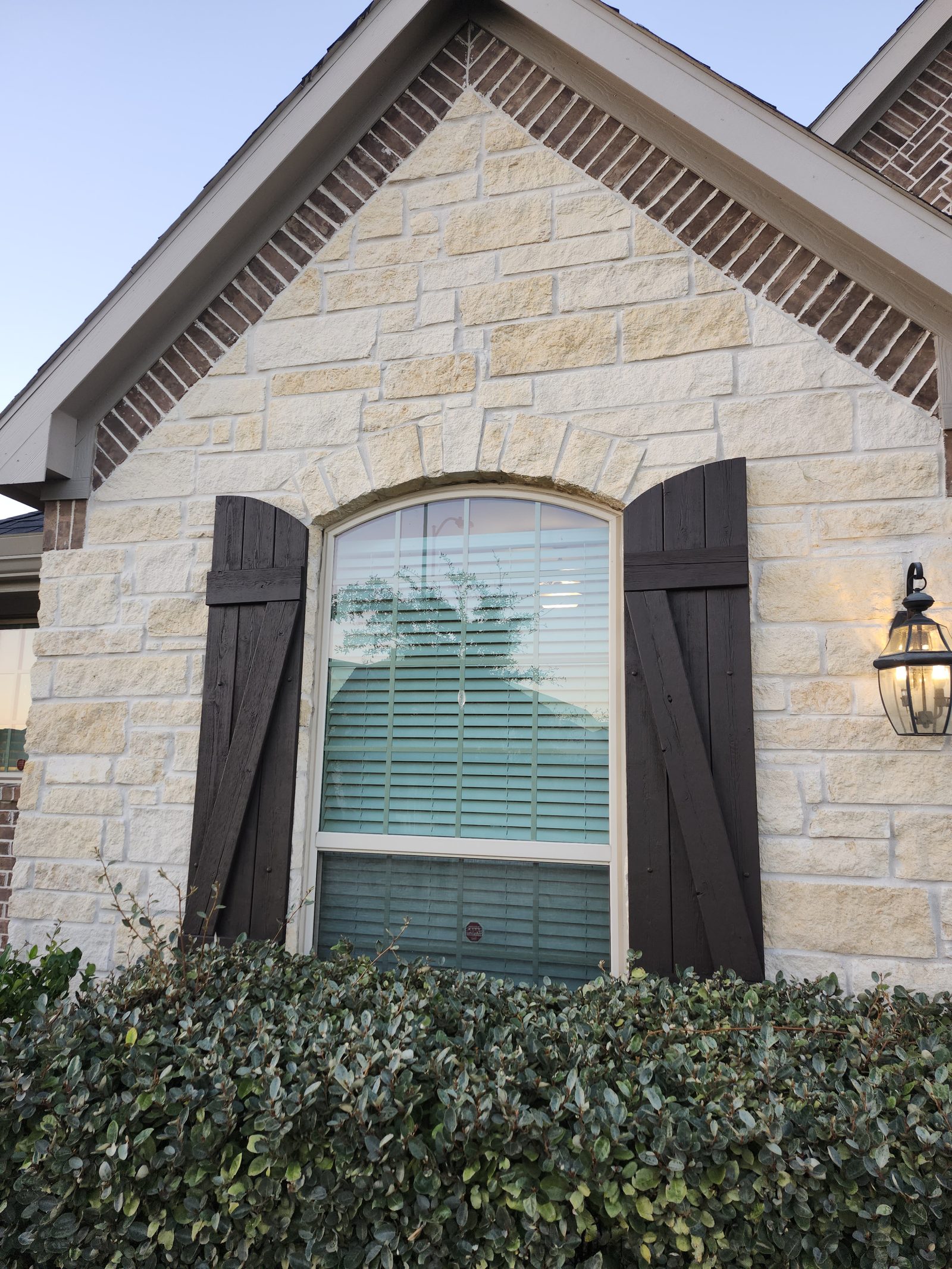 Dark stained wood shutters on a stone gable window in Katy, TX